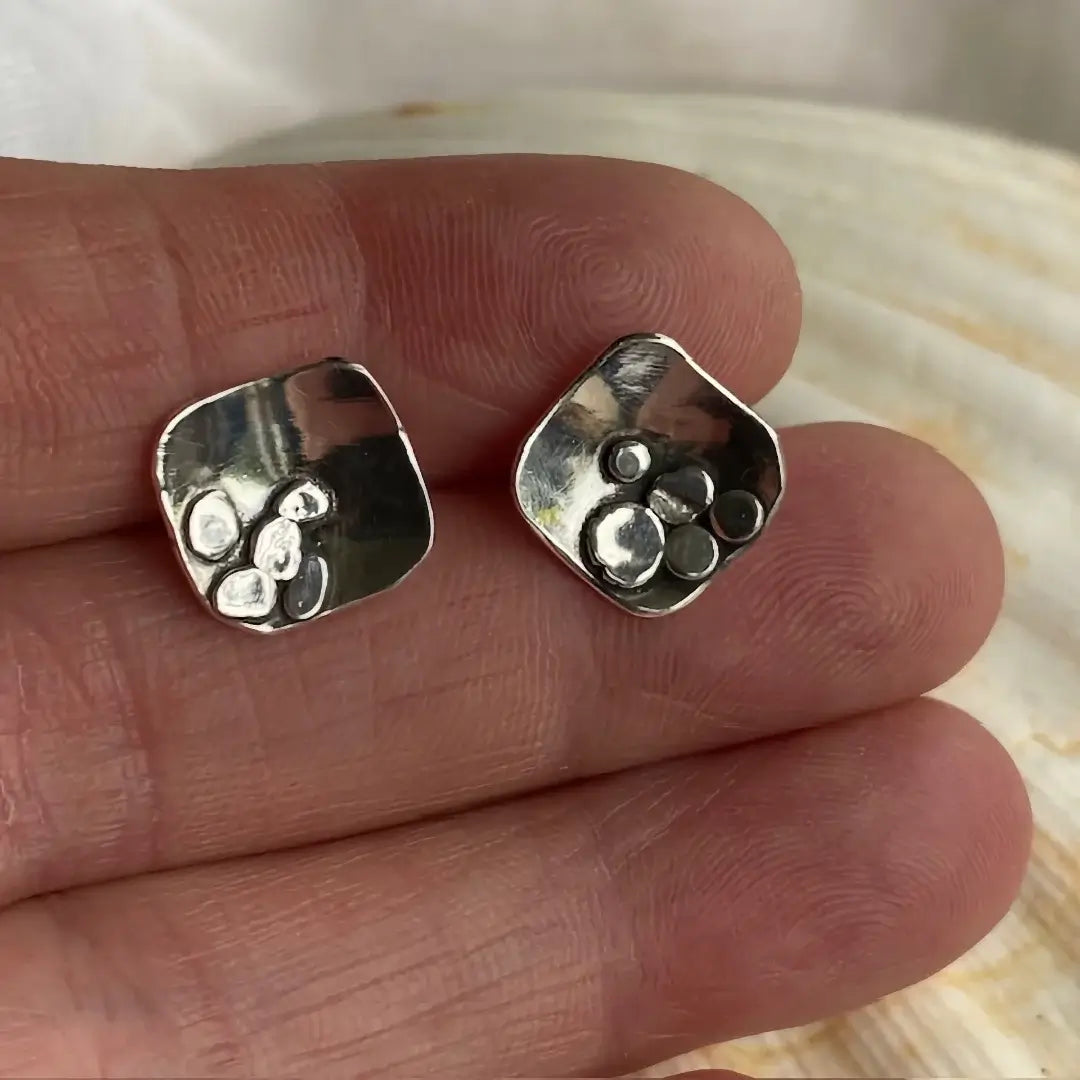 Silver earrings held between fingers with a shell background