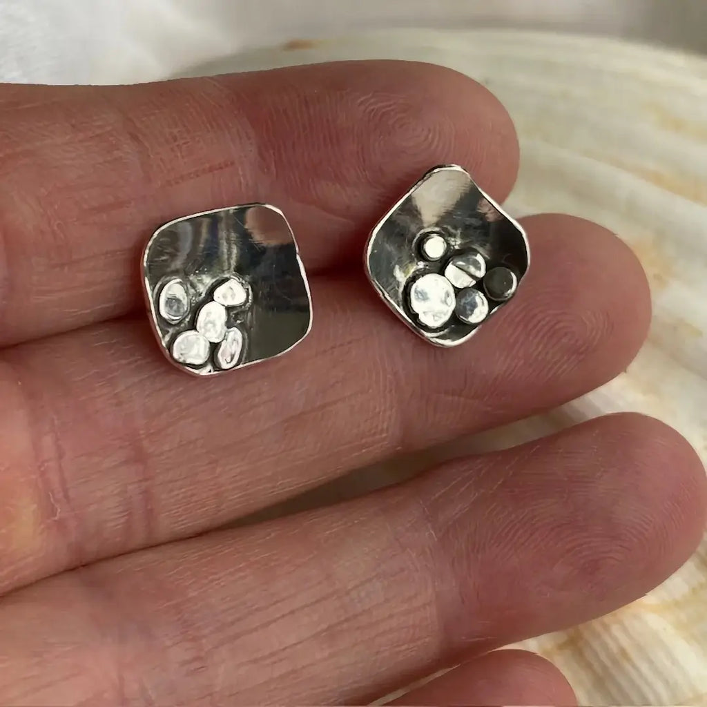 Silver earrings held between fingers with a shell background